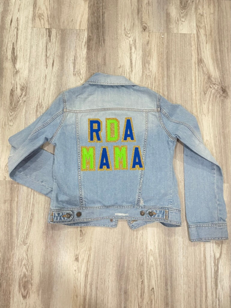 Denim jacket with 'RDA MAMA' text on a wooden surface