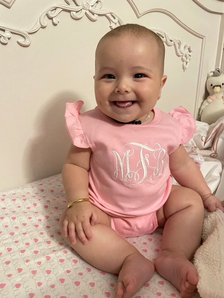 Baby wearing a pink outfit with 'MFB' Embroidered on the front of the bodysuit