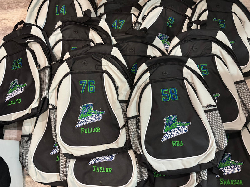 Collection of backpacks with ebroidered gator logo, numbers and names on a wooden floor.