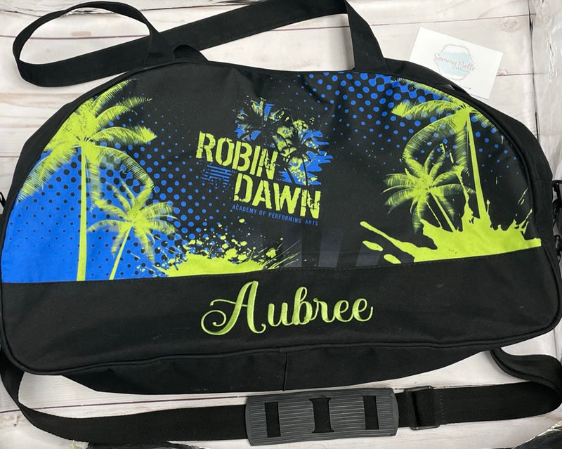 Black duffel bag with palm tree design and text on a wooden surface