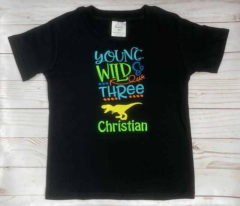 Black t-shirt with colorful text and dinosaur graphic on a wooden surface
