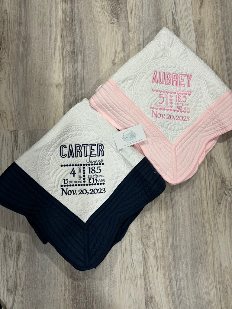 Two personalized baby blankets with embroidered names and dates on a wooden surface.