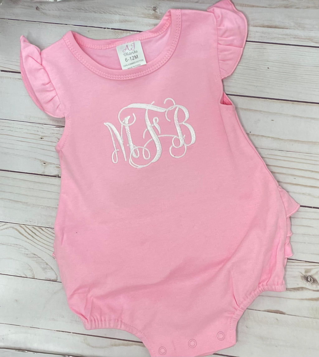 Pink baby romper with ruffled sleeves and 'MFB' monogram on a wooden surface