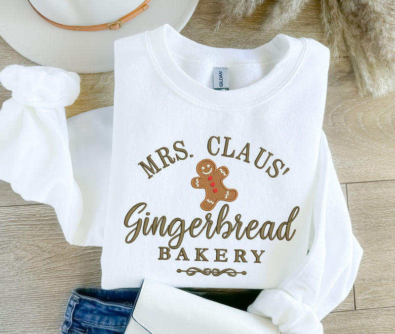 White sweatshirt with 'Mrs. Claus' Gingerbread Bakery' text and gingerbread man graphic on a wooden surface.
