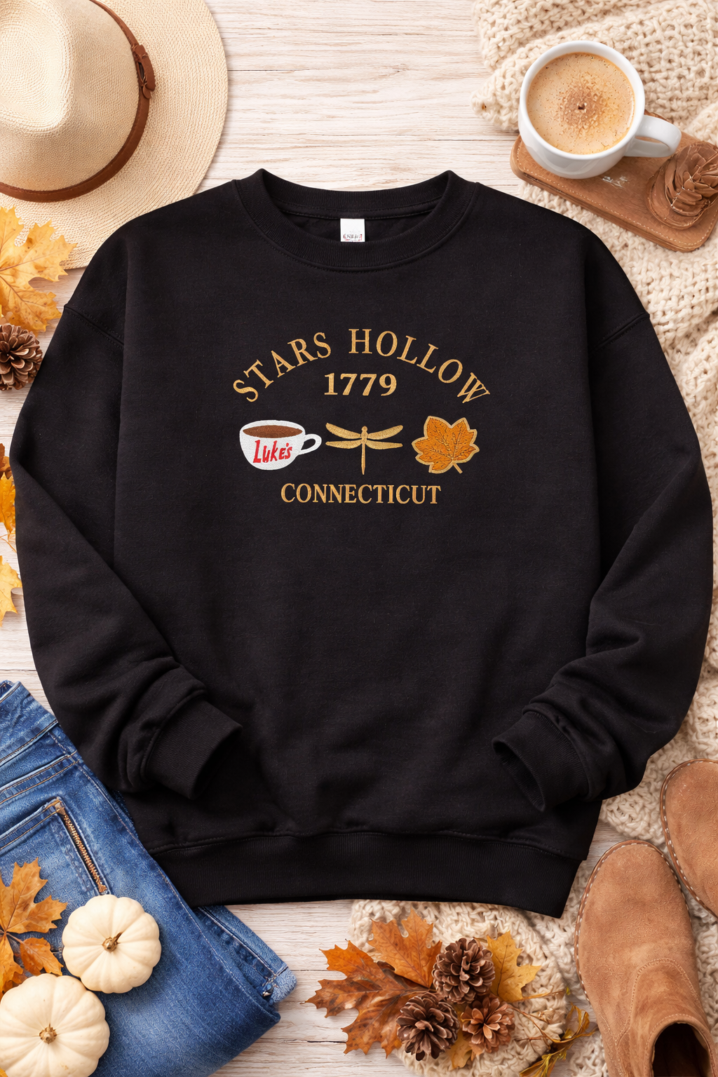 Black sweatshirt with 'Stars Hollow 1779 Connecticut' design on a wooden surface with autumn decorations.