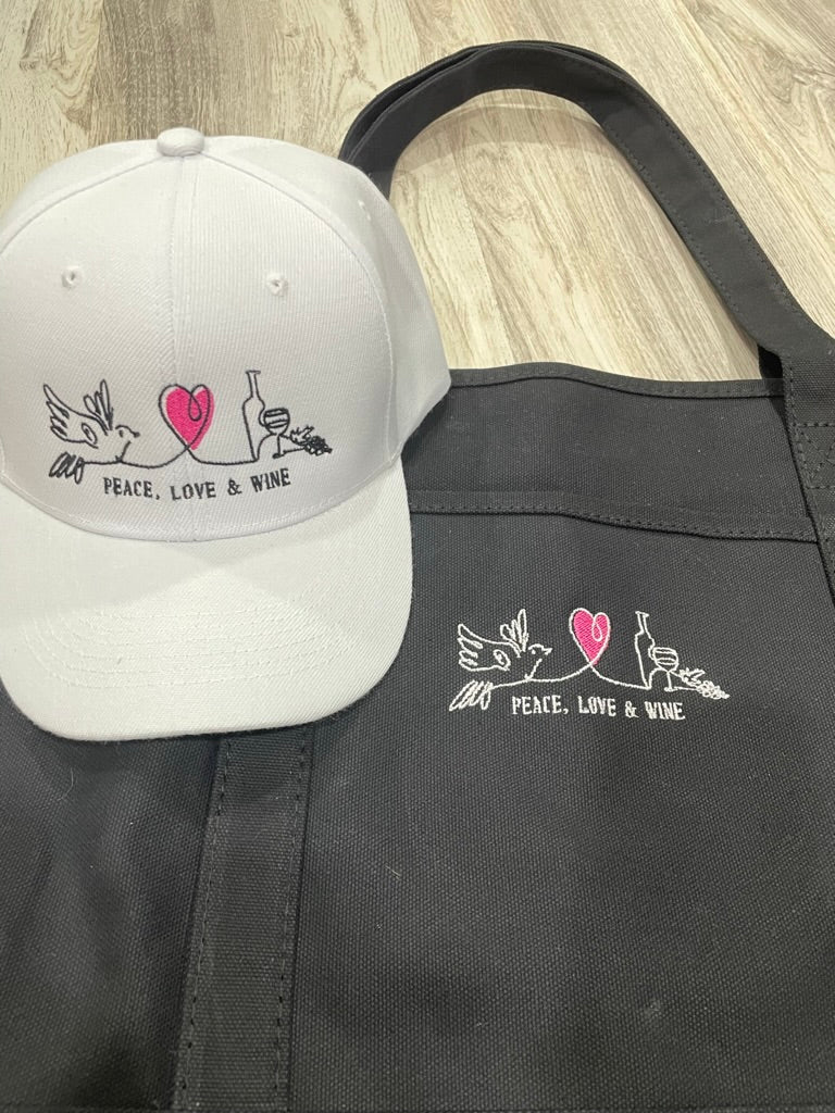 White cap and black apron with 'Peace, Love & Wine' design on a wooden surface
