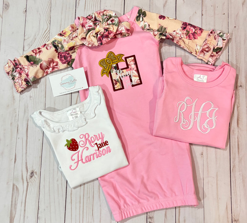 Collection of pink and white shirts with monogram designs on a wooden surface
