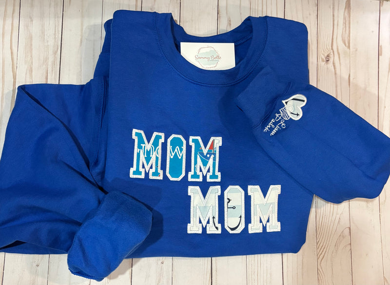 Blue sweatshirt with 'MOM' text on a wooden surface