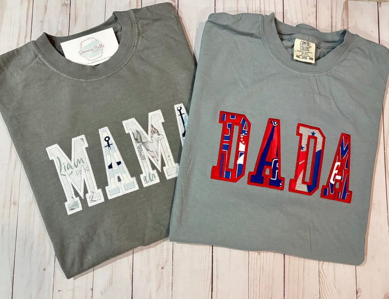 Two folded gray t-shirts with 'MAMA' and 'DADA' text designs on a wooden surface.